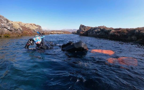 Snorkeler in Silfra fissure, Iceland, with clear blue water and rocky landscape.