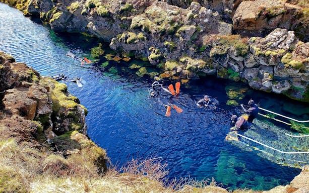Snorkelers in Silfra fissure, Iceland, surrounded by clear blue water and rocky landscape.