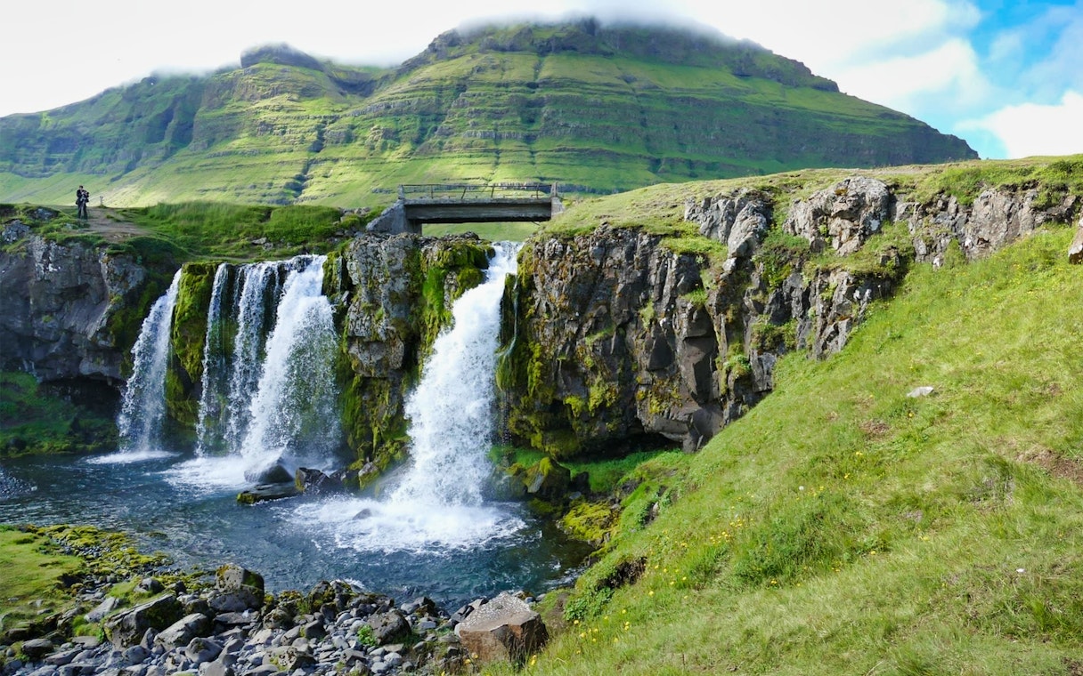 Waterfall on Snaefellsnes Peninsula with lush green cliffs and a mountain backdrop.