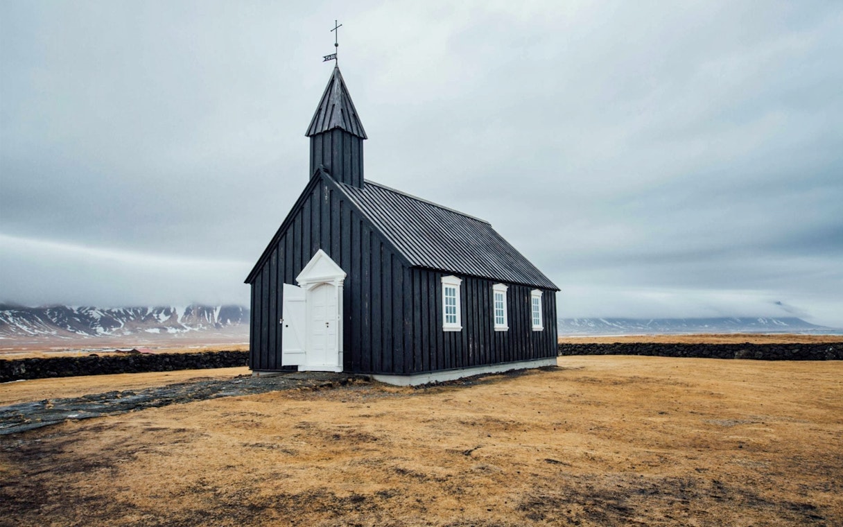 Black church on Snaefellsnes Peninsula with mountains in the background.
