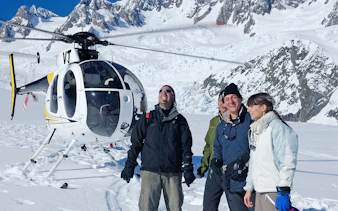 Helicopter tour group on snowy Fox Glacier with mountain backdrop.