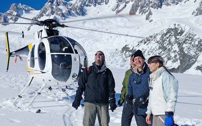 Helicopter tour group on snowy Fox Glacier with mountain backdrop.