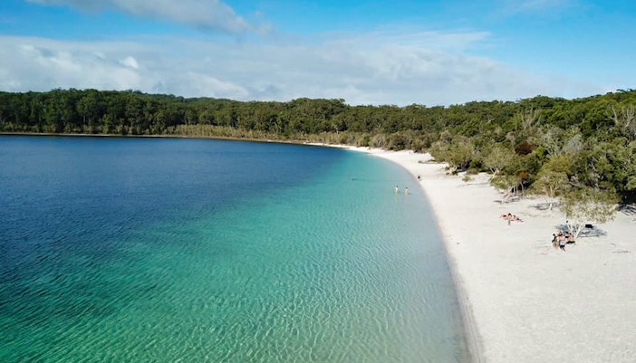 Fraser Island beach with clear water and forest backdrop on 4WD day tour.