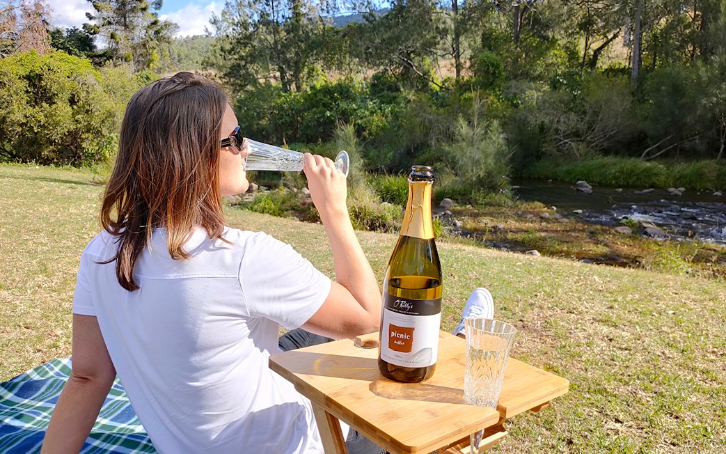 Woman sipping sparkling wine by a creek at O'Reilly's Vineyard.