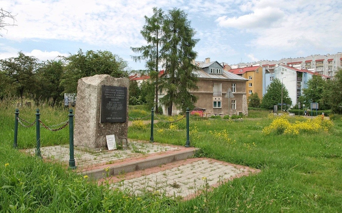 Memorial stone at Plaszow Concentration Camp site in Krakow, surrounded by greenery and buildings.