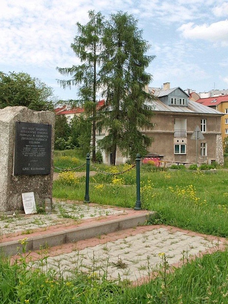 Memorial stone at Plaszow Concentration Camp site in Krakow, surrounded by greenery and buildings.