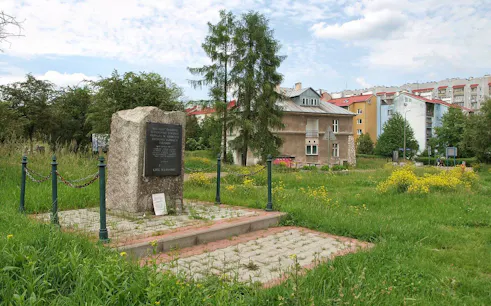 Memorial stone at Plaszow Concentration Camp site in Krakow, surrounded by greenery and buildings.