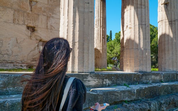 Visitor exploring Ancient Agora ruins with audio guide in hand.