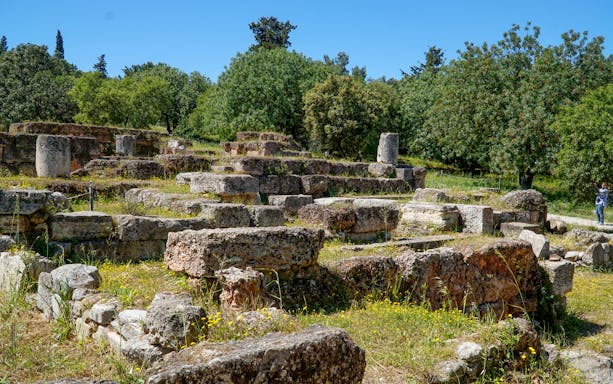 Ancient Agora ruins with stone foundations and greenery in Athens, Greece.