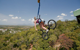 Person bungy jumping with a bicycle over lush landscape in Cairns, Australia.