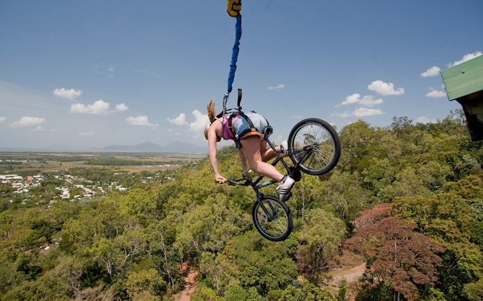 Person bungy jumping with a bicycle over lush landscape in Cairns, Australia.