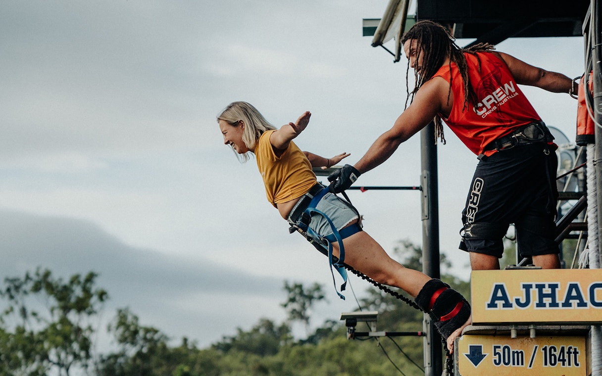 Person bungy jumping from platform in Cairns, Australia, assisted by crew member.