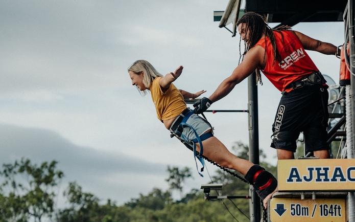 Person bungy jumping from platform in Cairns, Australia, assisted by crew member.