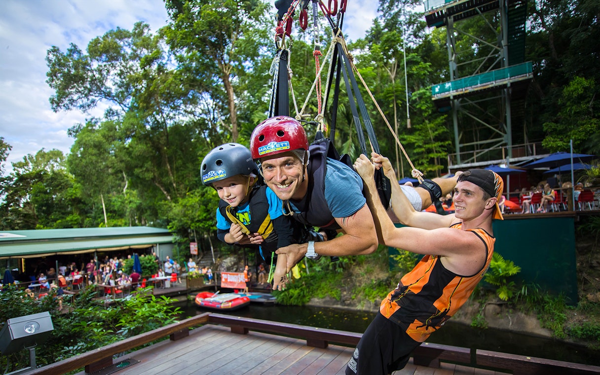 Participants on the Cairns Giant Swing, suspended in harnesses, surrounded by lush greenery.