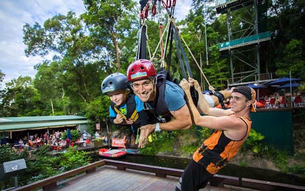 Participants on the Cairns Giant Swing, suspended in harnesses, surrounded by lush greenery.