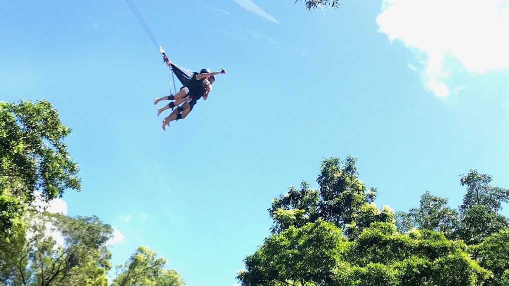 Skypark Cairns visitors on a giant swing above lush trees.