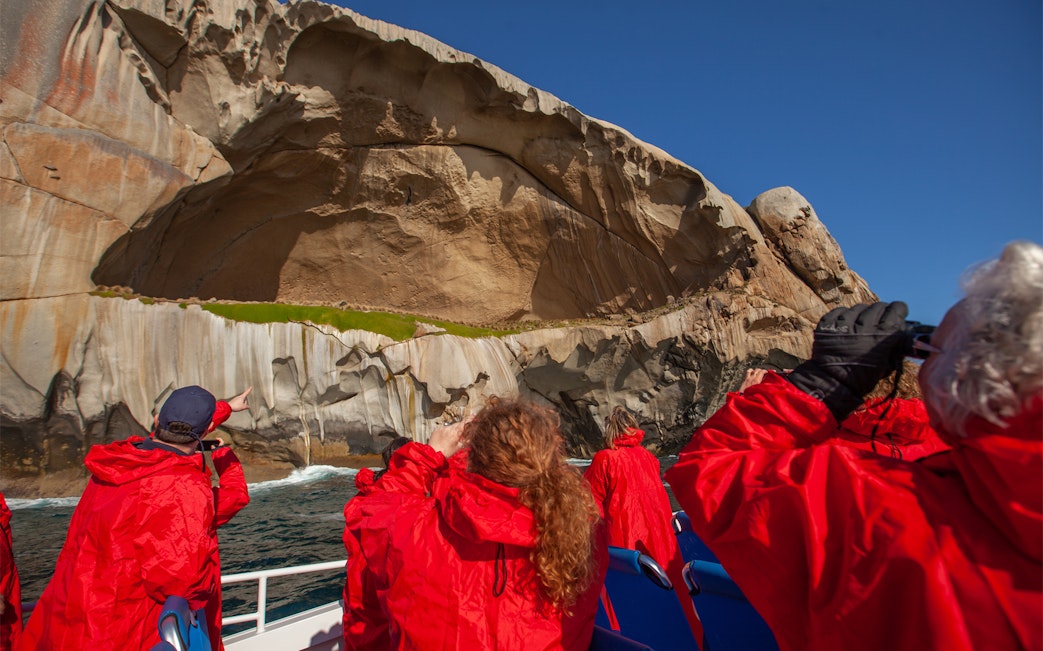 Tourists in red jackets viewing rock formations on a Wilsons Promontory cruise, Australia.
