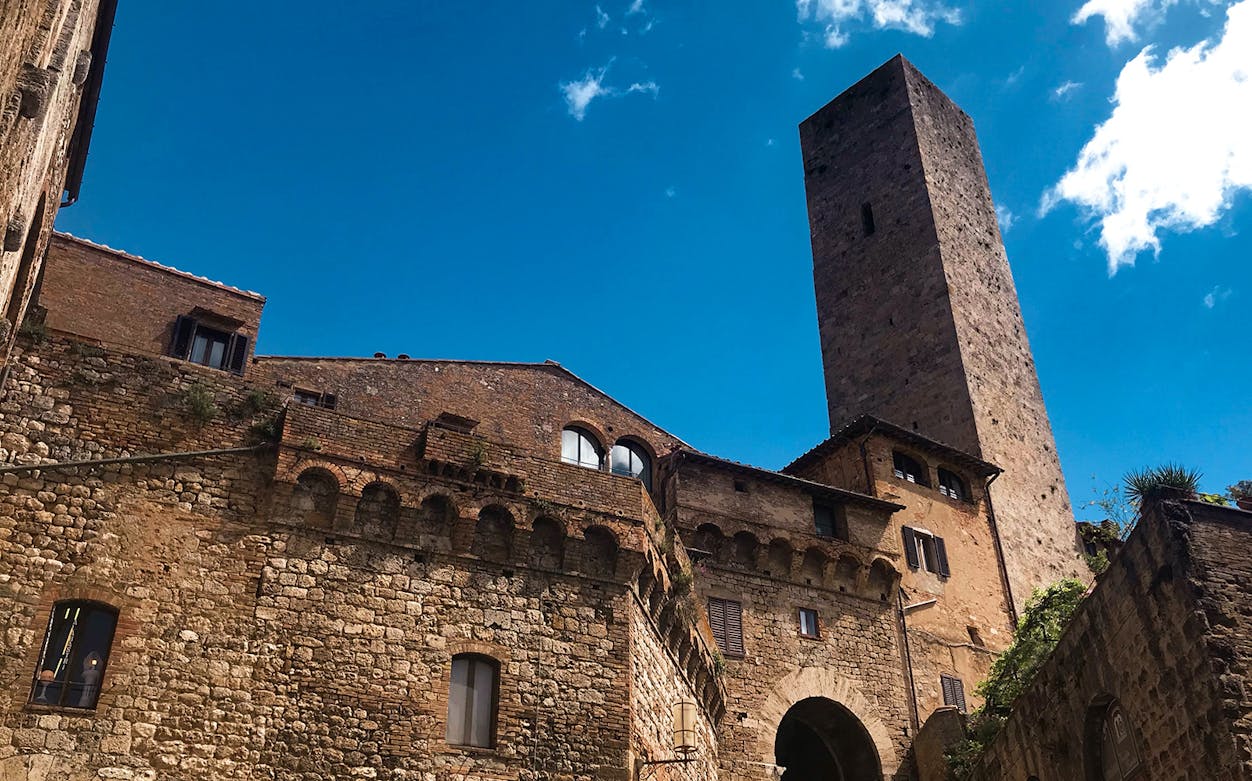San Gimignano stone tower and historic buildings under blue sky.