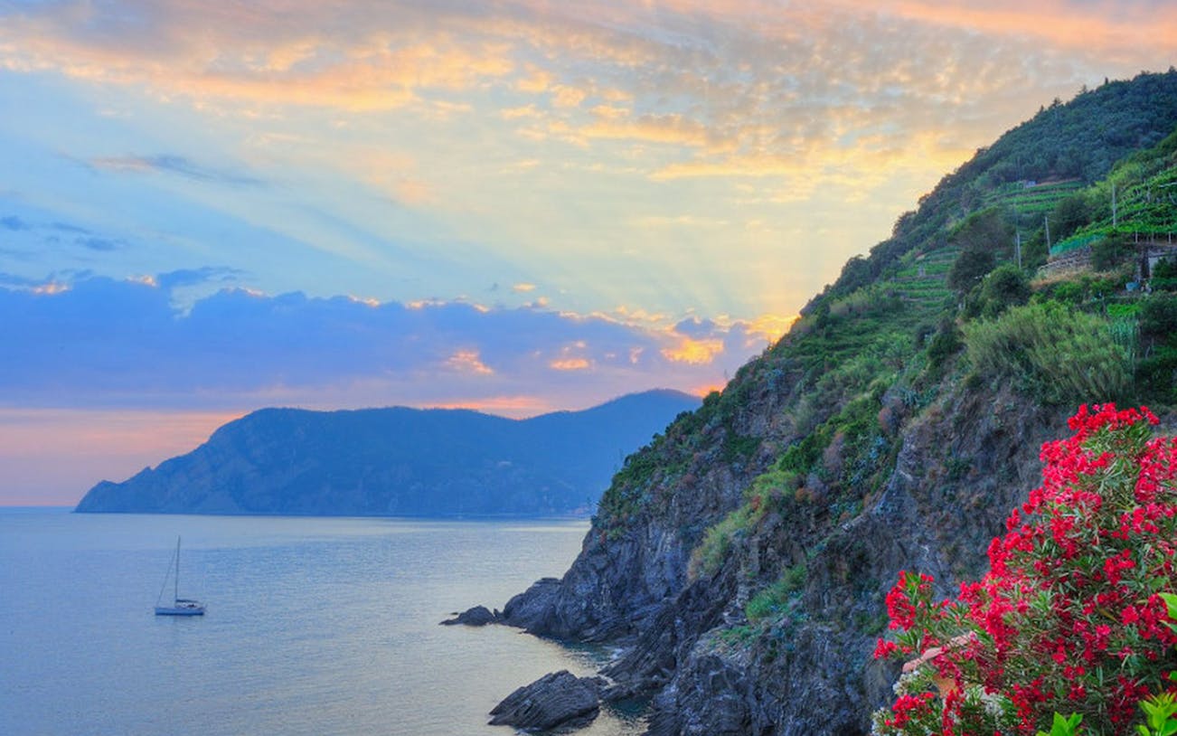Sunset over the cliffs and sea in Cinque Terre, Italy, with a sailboat near Riomaggiore.