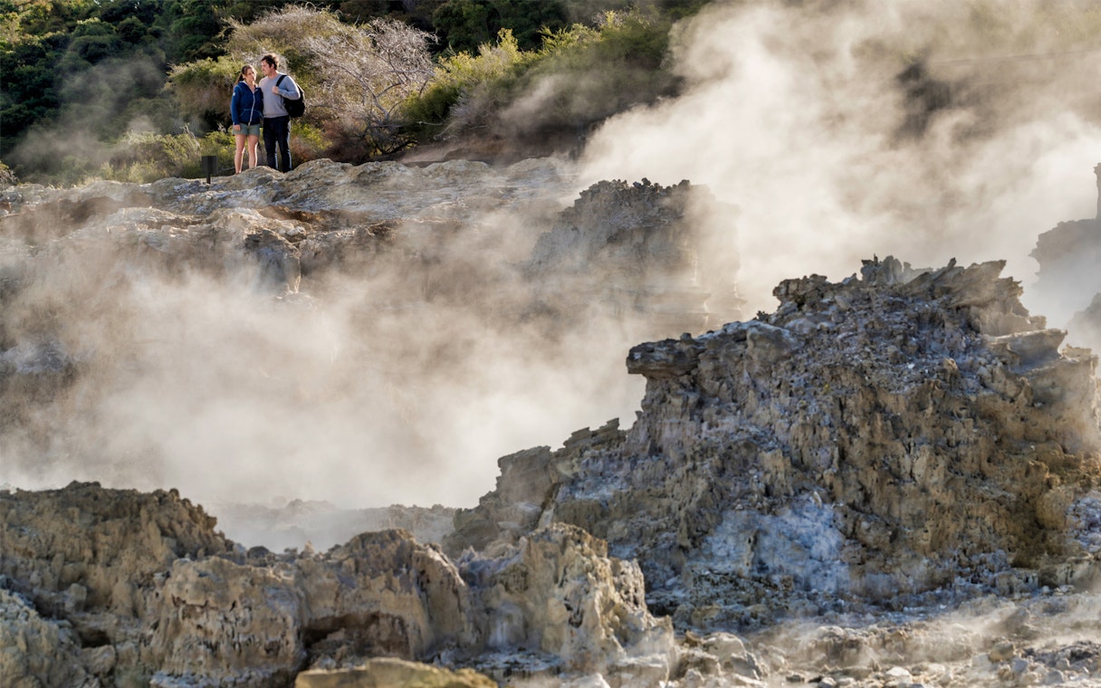 Couple standing amidst geothermal steam at Hell's Gate, New Zealand.