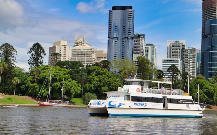 Cruise boat on Brisbane River with city skyline in background.