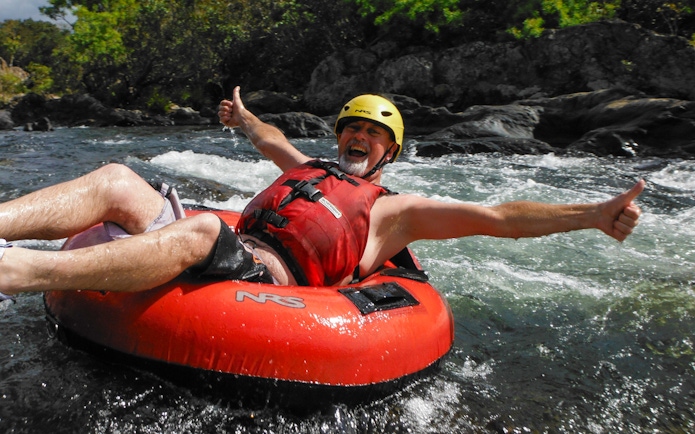 Man enjoying river tubing adventure with thumbs up in a rapid stream.