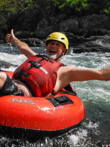Man enjoying river tubing adventure with thumbs up in a rapid stream.