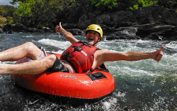 Man enjoying river tubing adventure with thumbs up in a rapid stream.