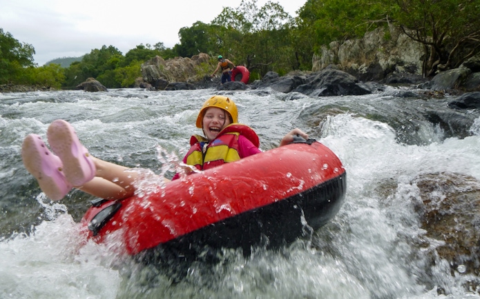 Child enjoying river tubing adventure through rapids, wearing safety gear.