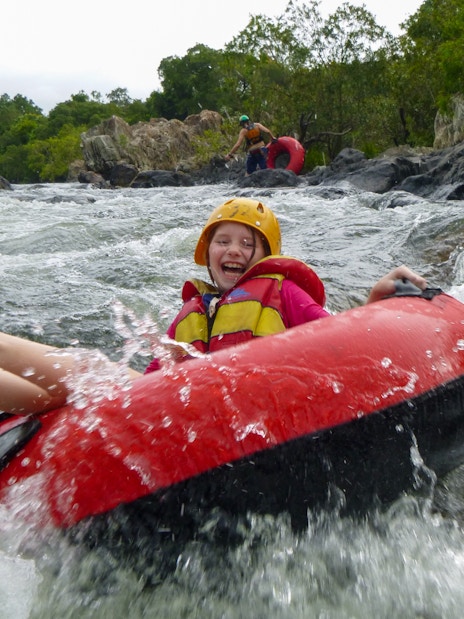 Child enjoying river tubing adventure through rapids, wearing safety gear.
