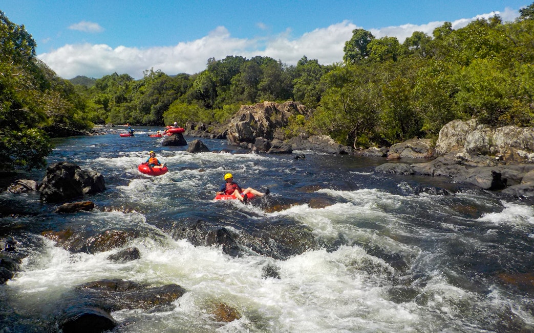 People tubing down a rocky river surrounded by lush greenery.