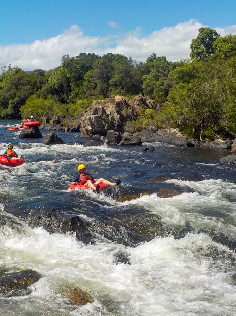 People tubing down a rocky river surrounded by lush greenery.