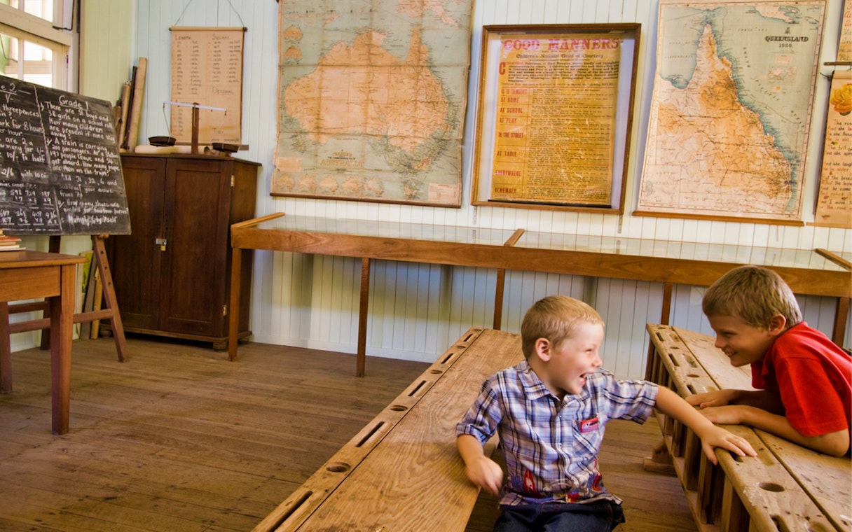 Children in a historic classroom at Herberton Historic Village, Australia, with vintage maps and chalkboard.