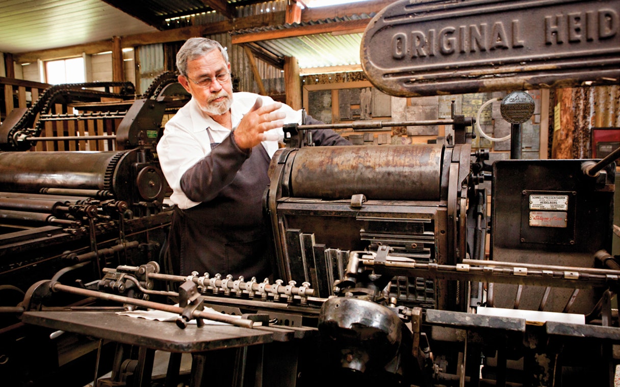 Man operating vintage printing press at Herberton Historic Village.