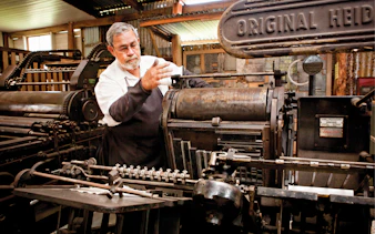 Man operating vintage printing press at Herberton Historic Village.