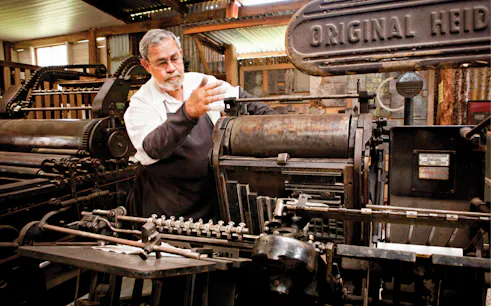 Man operating vintage printing press at Herberton Historic Village.