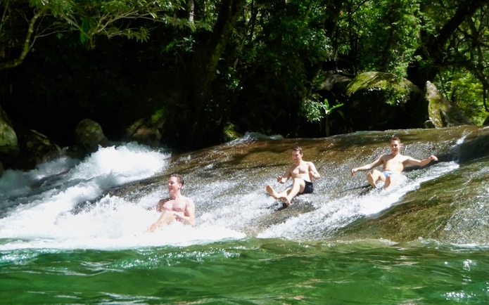 Visitors sliding down a natural rock slide at Atherton Tablelands waterfalls during a tour from Cairns.