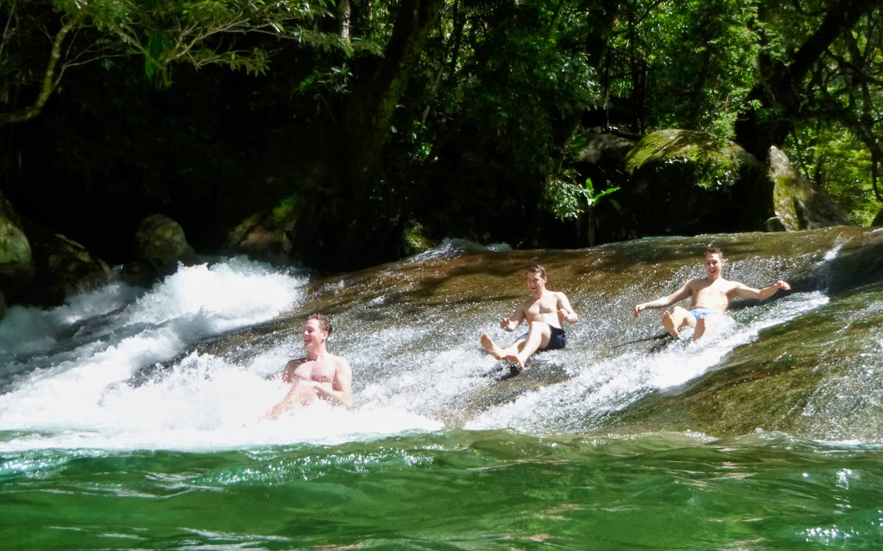 Visitors sliding down a natural rock slide at Atherton Tablelands waterfalls during a tour from Cairns.