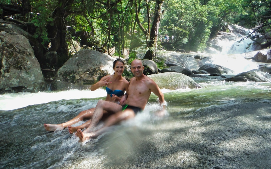 Couple enjoying a natural rock slide at Atherton Tablelands waterfall near Cairns.