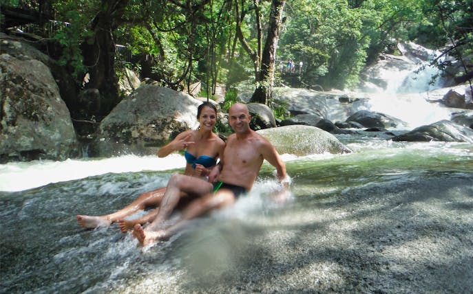 Couple enjoying a natural rock slide at Atherton Tablelands waterfall near Cairns.