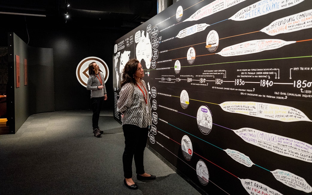Visitors examining historical timeline at Port Arthur Historic Site exhibit.