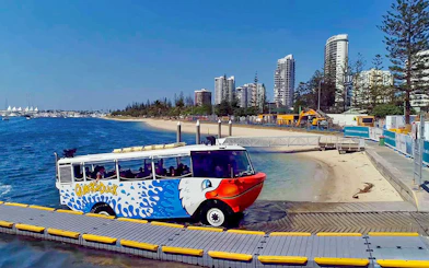 Quack'R Duck amphibious vehicle entering water at Gold Coast with city skyline in background.