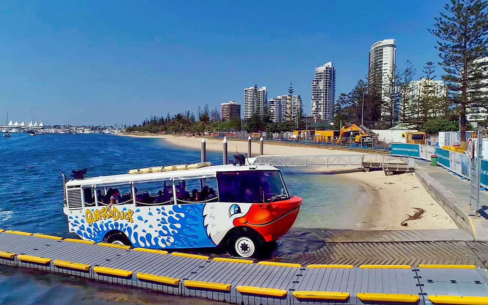 Quack'R Duck amphibious vehicle entering water at Gold Coast with city skyline in background.