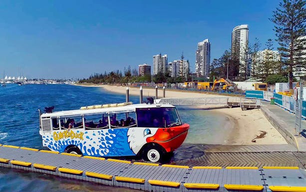 Quack'R Duck amphibious vehicle entering water at Gold Coast with city skyline in background.