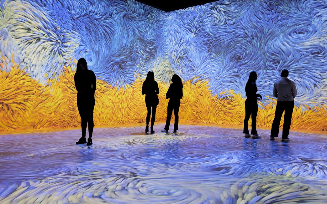 Visitors immersed in swirling blue and yellow digital art at an audiovisual experience.