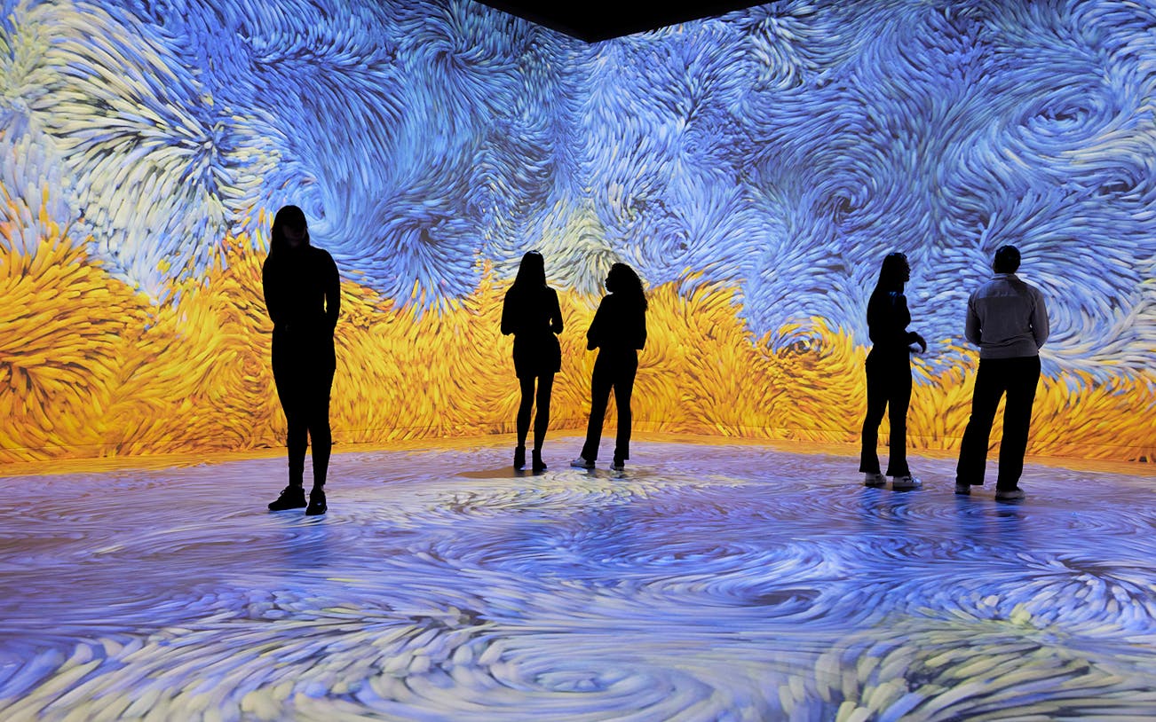 Visitors immersed in swirling blue and yellow digital art at an audiovisual experience.