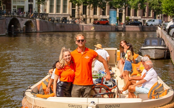 Amsterdam canal cruise with people enjoying drinks on an open boat.