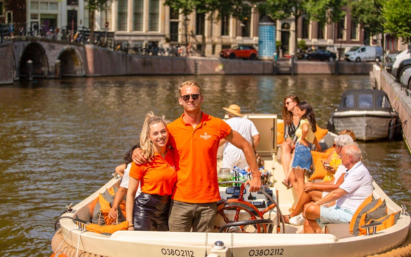 Amsterdam canal cruise with people enjoying drinks on an open boat.