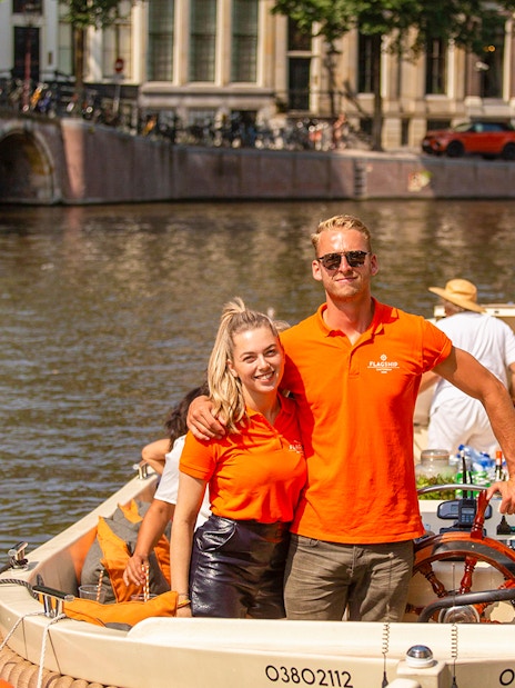 Amsterdam canal cruise with people enjoying drinks on an open boat.