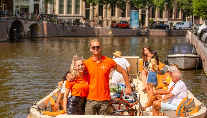 Amsterdam canal cruise with people enjoying drinks on an open boat.
